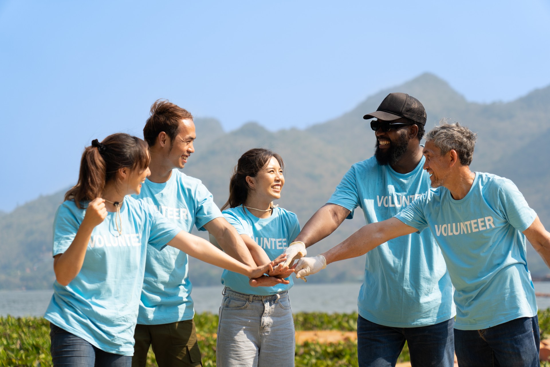 Group of happy diverse volunteers joining stacked hands together with smiles